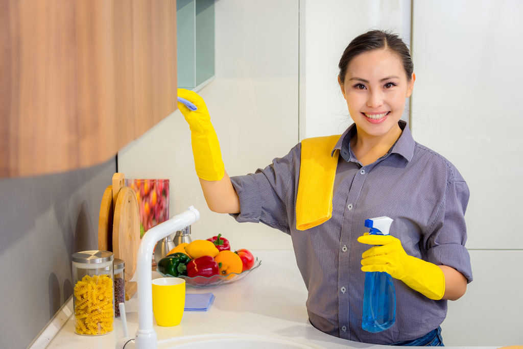 A woman meticulously cleaning cabinet .