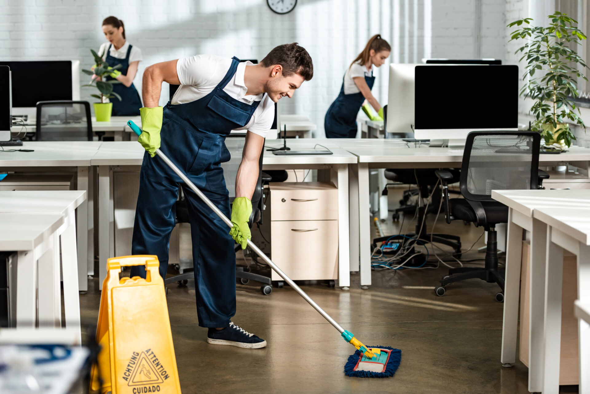 young, smiling cleaner washing floor with mop in modern office