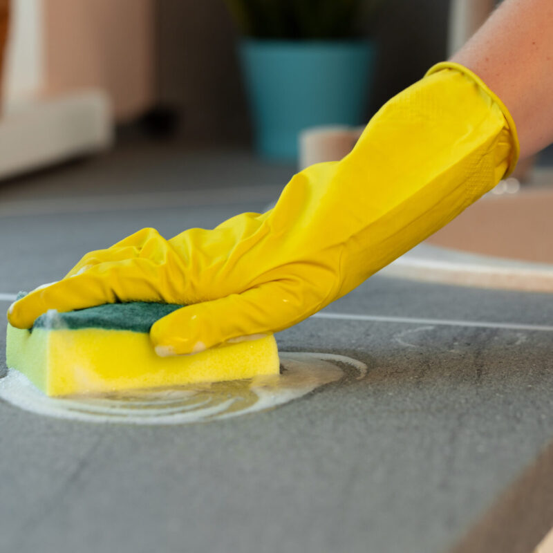 Woman's hands in yellow gloves cleaning counter top in kitchen close up